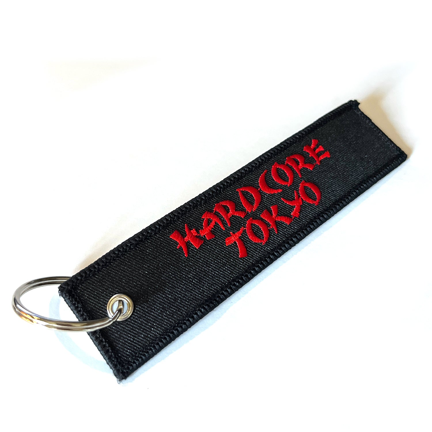 Black fabric keychain with red text 'Hardcore Tokyo' in oriental font