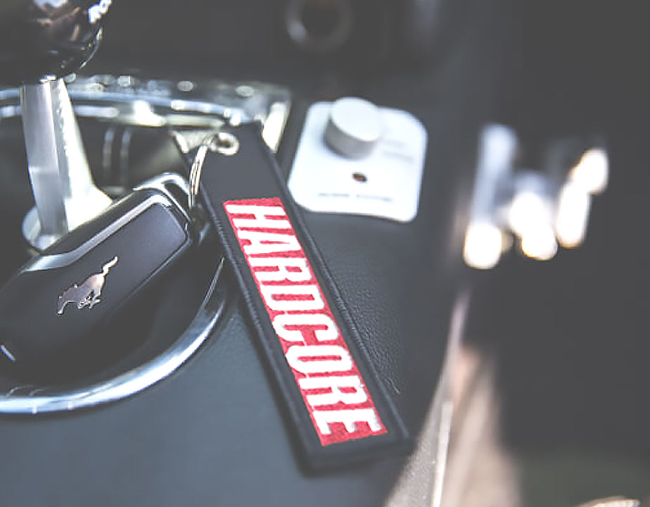 Black fabric keychain with 'HARDCORE' text logo as a Red box with White Text.