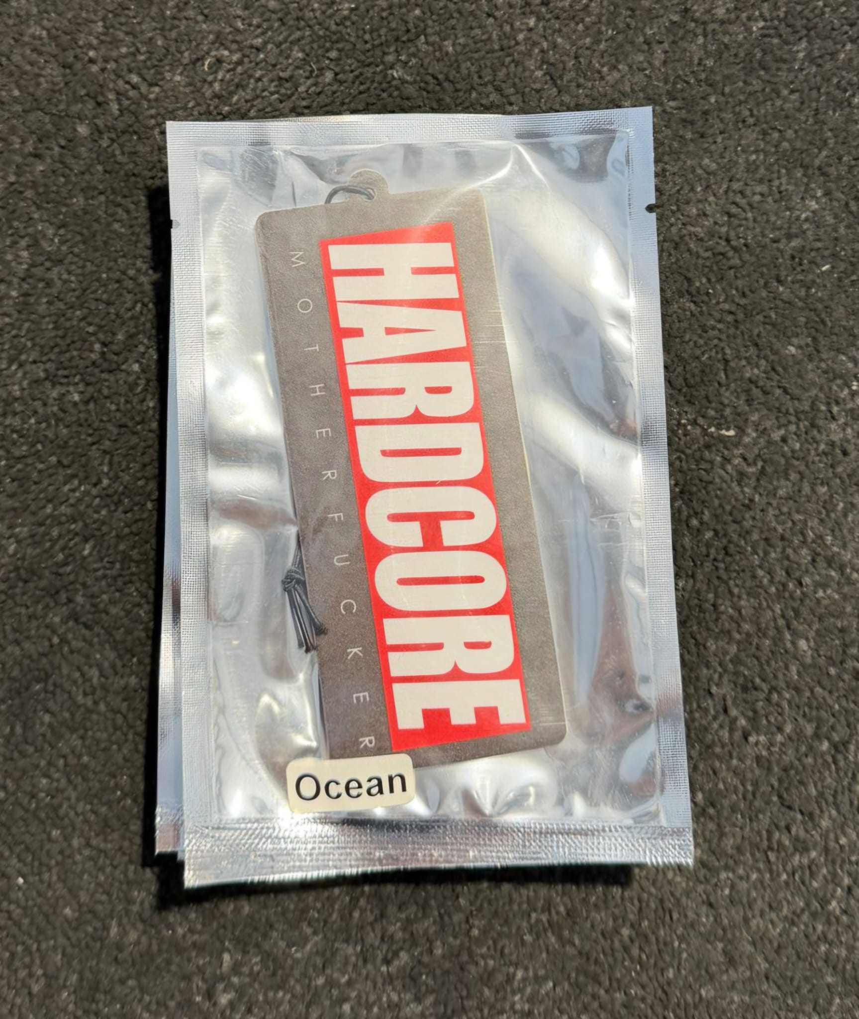 Clear plastic packaging with 'Hardcore' label on a dark surface. Hardcore Tokyo Logo Air Freshener with an Ocean Flavour